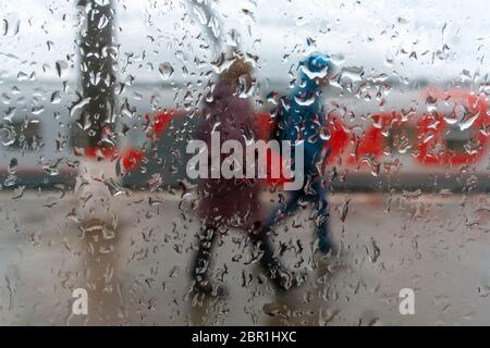 Les passagers marchent à la gare. Vue à travers le verre avec gouttes de pluie dessus. Banque D'Images