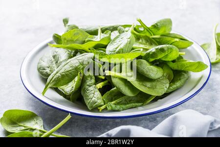 Feuilles d'épinards pour bébés dans un bol sur fond gris en béton, vue de dessus, espace de copie. Manger propre, détox, ingrédient alimentaire Banque D'Images