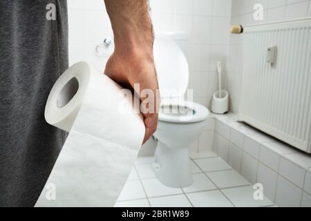 L'homme souffre de diarrhée Rouleau de papier tissu tenant debout devant la cuvette des toilettes Banque D'Images