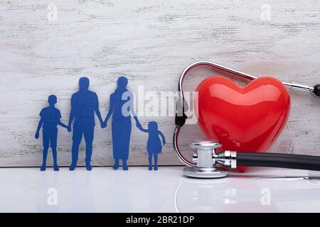 Close-up d'une famille avec le stéthoscope et forme de coeur rouge en face du mur en bois Banque D'Images