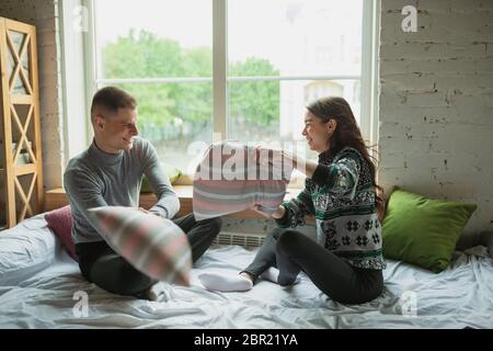 Les oreillers se battent, s'amuser. Quarantaine verrouillage, séjour à la maison concept - jeune beau couple appréciant un nouveau style de vie pendant le coronavirus urgence sanitaire mondiale. Bonheur, ensemble, santé. Banque D'Images