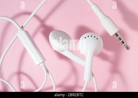 écouteurs intra-auriculaires blancs sur fond rose clair. Vue de dessus fermée. Banque D'Images