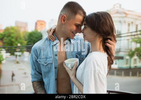 Sur le balcon, charmant. Confinement de quarantaine, concept de séjour à la maison - jeune beau couple caucasien appréciant un nouveau style de vie pendant l'urgence de santé du coronavirus. Bonheur, ensemble, santé. Banque D'Images