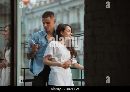 Sur le balcon, élégant. Confinement de quarantaine, concept de séjour à la maison - jeune beau couple caucasien appréciant un nouveau style de vie pendant l'urgence de santé du coronavirus. Bonheur, ensemble, santé. Banque D'Images