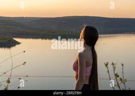 Jeune femme aux longs cheveux brunette, vêtue de soutien-gorge rose regardant au loin, les montagnes et la rivière sur le fond Banque D'Images