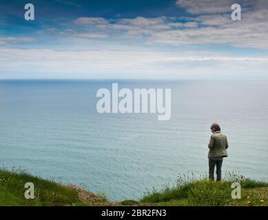 Vue arrière d'une femme non identifiée se tenant sur une falaise et regardant la mer en Irlande Banque D'Images