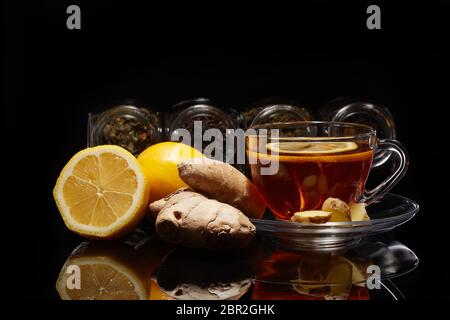 Diverses sortes de thé sec dans des bocaux en verre et tasse de thé aromatique avec du gingembre et citron debout sur un fond noir. Différents types de feuilles de thé. Banque D'Images