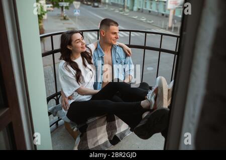 Assis sur le balcon, en riant. Quarantaine verrouillage, séjour à la maison concept - jeune beau couple caucasien appréciant un nouveau style de vie pendant le coronavirus. Bonheur, ensemble, santé. Banque D'Images