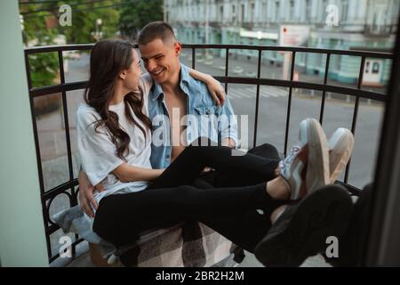 Assis sur le balcon, enserrer, regarder des séries. Quarantaine verrouillage, séjour à la maison concept - beau couple caucasien appréciant un nouveau style de vie pendant le coronavirus. Bonheur, ensemble, santé. Banque D'Images