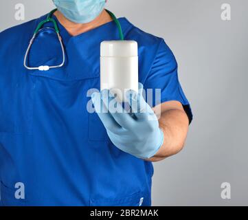 Médecin en uniforme bleu organise un pot plastique blanc avec des comprimés, fond gris Banque D'Images