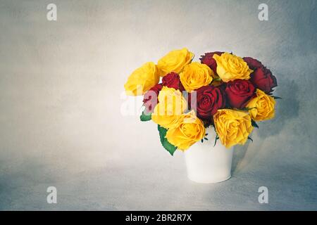 Bouquet de roses rouges et jaunes dans un vase blanc. Image en tons. Copier l'espace. Arrière-plan des fêtes. Copier l'espace pour le texte Banque D'Images