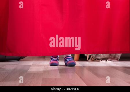 La section basse d'un Girl's pieds derrière le rideau sur plancher de bois franc Banque D'Images