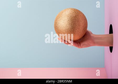 Main de femme tenant une boule dorée sur fond rose et bleu Banque D'Images