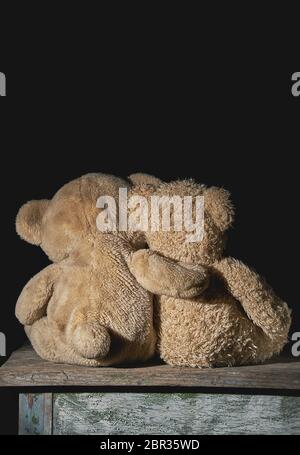 Deux vieux nounours brun hugging assis sur une surface en bois, les jouets s'en retourna, fond noir Banque D'Images