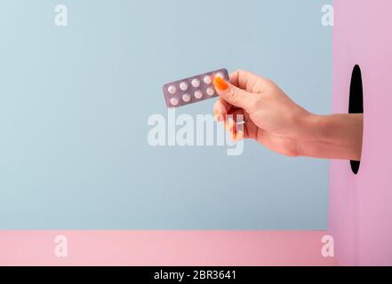 Main de femme tenant une plaquette de pilules sur fond bleu et rose Banque D'Images