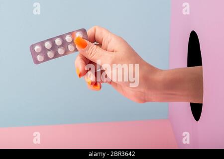 Gros plan sur la main de la femme tenant une plaquette de pilules sur fond bleu et rose Banque D'Images