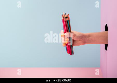 Main de femme tenant un ensemble de crayons de couleur sur fond bleu et rose Banque D'Images