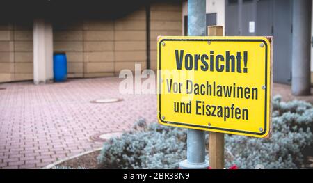 Attention ! Dans l'avant du toit, les avalanches et de glaçons en allemand sur un panneau jaune en face d'un bâtiment Banque D'Images