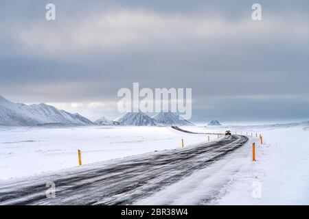 Route principale islandaise en hiver coupant à travers un paysage montagneux, volcanique, enneigé. Avec la voiture approchant dans la distance Banque D'Images