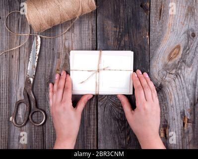 Les mains tenant les vieux papiers cartes postales liés avec une corde sur fond de bois gris, vue du dessus Banque D'Images