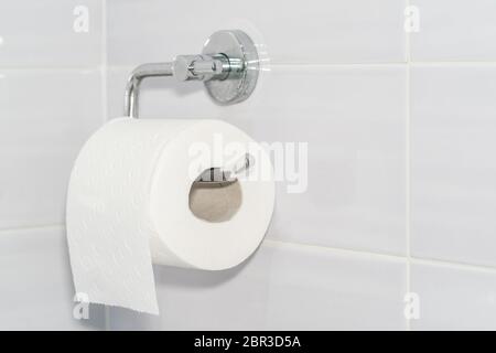 Gros plan d'un rouleau de papier toilette blanc et doux accroché à un support moderne en chrome dans une salle de bain lumineuse. Banque D'Images