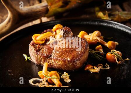 La partie épaisse de la venaison sauvage grillé Steak de cerf avec l'automne les champignons et les oignons frits servi dans une casserole de métal dans une vue en gros convient pour un menu Banque D'Images