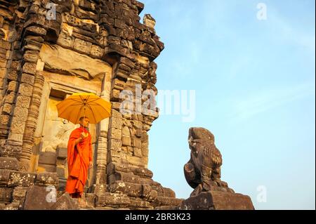 Un Monk se tient avec un parasol devant un temple à Roluos. Angkor, site du patrimoine mondial de l'UNESCO, province de Siem Reap, Cambodge, Asie du Sud-est Banque D'Images