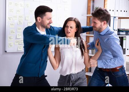 Close-up des hommes d'entrer dans une lutte femme essayant de les séparer dans Office Banque D'Images