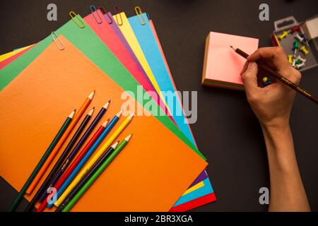 Retour à l'école. Crayons, papier multicolore et trombones sur fond noir Banque D'Images