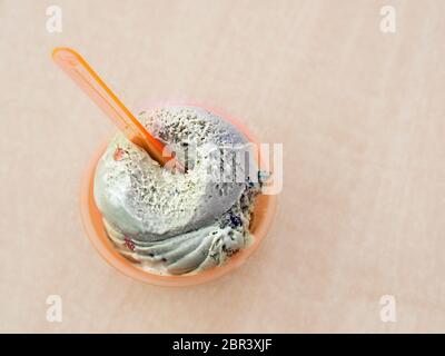 Une portion de crème glacée, la saveur pistache, dans un pot en plastique de couleur orange. En haut il y a une cuillère en plastique dans la même couleur à l'intérieur. En vue supérieure, avec p Banque D'Images