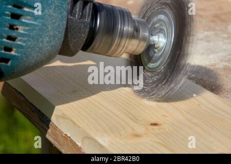 Le processus de brossage de la planche en bois. La main mâle tient la machine à brosser tournant électrique avec la brosse disque métal ponçage un morceau de bois. Banque D'Images