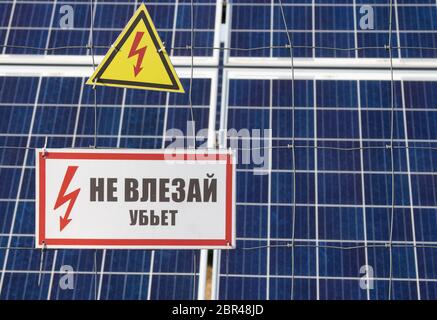 Station de ferme solaire sur un fond sélectif foyer sur un triangle jaune d'avertissement haute tension. L'inscription en russe n'est pas proche Banque D'Images