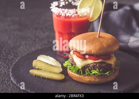 Hamburger avec un verre de jus de tomates sur le bord de la pierre noire Banque D'Images