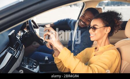 Couple afro-américain faisant Selfie assis dans une voiture nouvelle, Panorama Banque D'Images