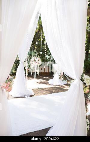 Décorations blanches pour la cérémonie de mariage à l'intérieur. Arc de mariage blanc avec fleurs et tapis blanc sur le sol et tissu blanc. Banque D'Images