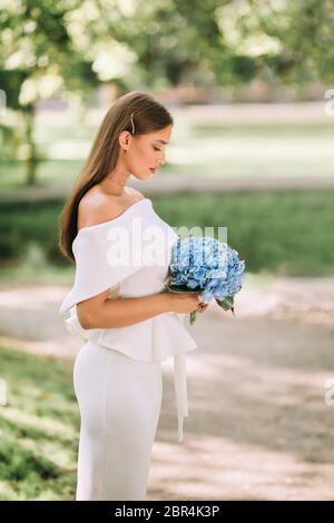 Robe élégante mariée blanche tenant le bouquet debout dans le parc Banque D'Images
