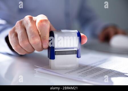 Close-up of a person's Hand Stamping avec timbre approuvé sur le document At Desk Banque D'Images