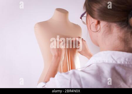 La couturière coupe le tissu avec de grandes ciseaux sur un mannequin. Banque D'Images