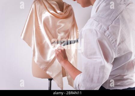 La couturière coupe le tissu avec de grandes ciseaux sur un mannequin. Banque D'Images