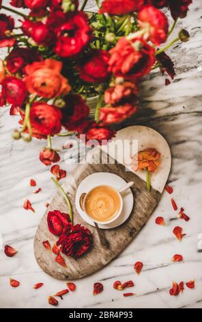 Plat-laque de tasse de café espresso noir sur la table de service et bouquet de fleurs de ranunculus rouges sur fond de table en marbre blanc plein de pétales, dessus Banque D'Images