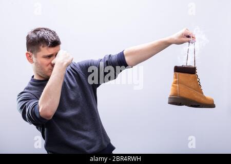 Portrait d'un homme portant sur son nez tout en maintenant ses chaussures puantes contre fond blanc Banque D'Images