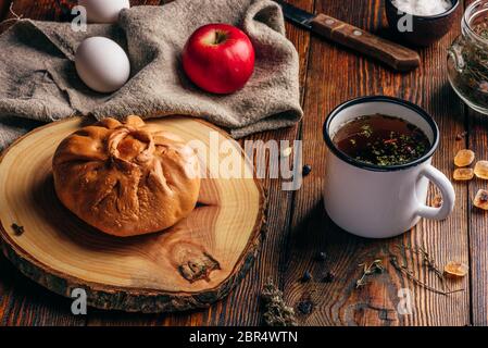 Petit-déjeuner rustique traditionnelle pâtisserie elesh avec tatar, tisane dans une tasse de métal, apple et œufs durs sur la surface en bois foncé Banque D'Images