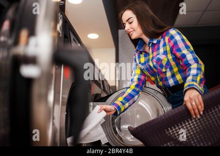 Une jeune fille sort les vêtements lavés d'un lave-linge Banque D'Images