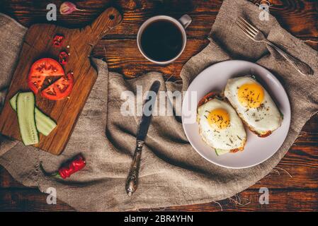 Petit-déjeuner toasts avec légumes et œufs frits sur plaque blanche et tasse de café plus de gray tissu rugueux. Vue de dessus. Banque D'Images