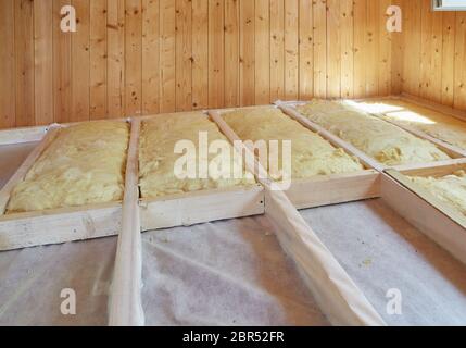 Pose de la couche d'isolation thermique sous le plancher avec de la laine minérale dans la chambre de la maison de campagne. Réchauffement d'un sol étape par étape. Banque D'Images
