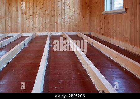 Installation de poutres longitudinales pour le réchauffement d'un plancher dans la maison de bois de campagne. Réchauffement d'un sol étape par étape. Banque D'Images