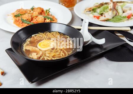 trois plats sur une table dans un restaurant, menu du café. Déjeuner d'affaires avec un bol de ramen avec poulet et œufs, salade césar fraîche et pâtes Banque D'Images