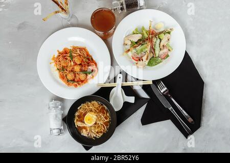 trois plats sur une table dans un restaurant, menu du café. Déjeuner d'affaires avec un bol de ramen avec poulet et œufs, salade césar fraîche et pâtes Banque D'Images