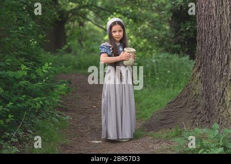 La jeune fille dans une robe de style rétro avec un pot en argile au milieu de la forêt. Banque D'Images