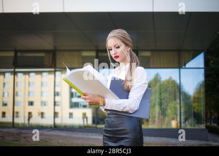 Une jeune femme d'affaires avec une expression faciale mécontente examine les documents en détail Banque D'Images